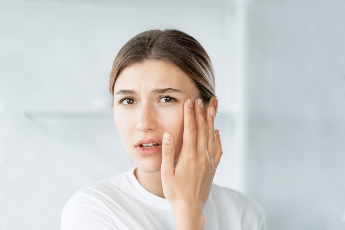 a woman holding a hand to her face and looking uncomfortable