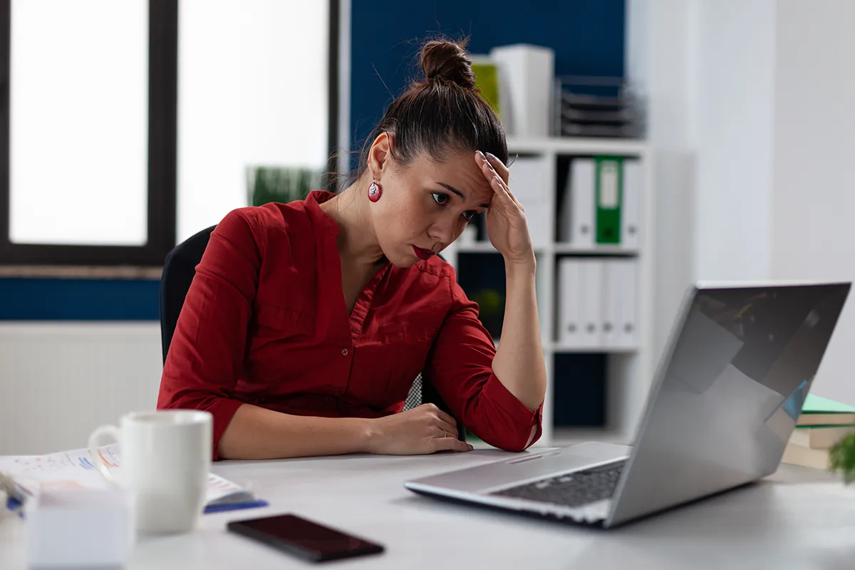 a tired woman sitting in her office and holding a hand to her head