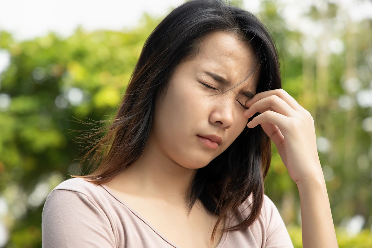 a woman outside holding a hand to her eye due to dry eye irritation
