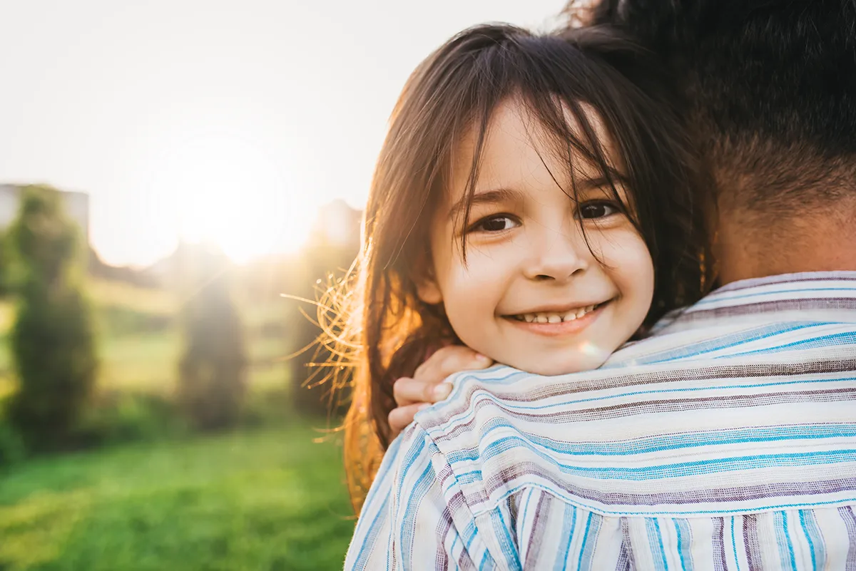 a little girl smiling and hugging her dad outdoors